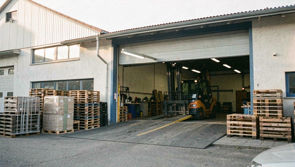 Gewerbebetrieb am Ortseingang mit Laderampe: Paletten, Gabelstappler und offenes Rolltor im Morgenlicht